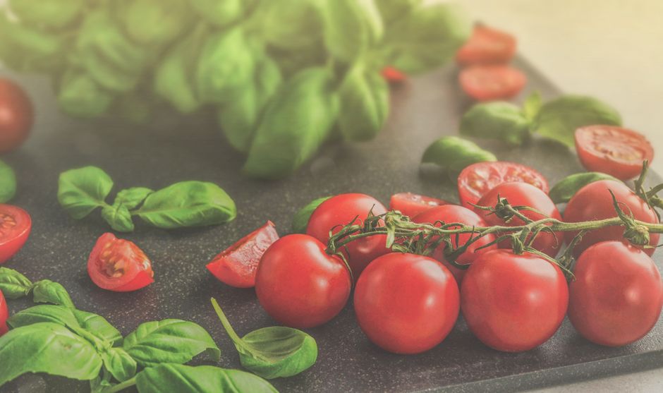 Close-up of vibrant green basil leaves and ripe red tomatoes on wooden surface